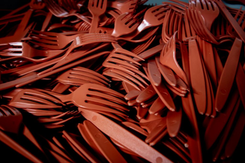 Detailed shot of red plastic forks and knives piled together. Perfect for recycling or waste concept.