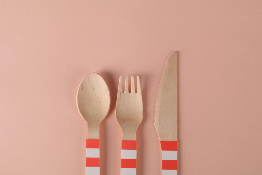Minimalist arrangement of eco-friendly wooden utensils on a pastel pink background.