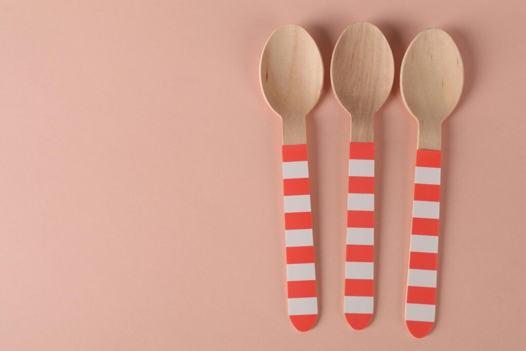 Three eco-friendly wooden spoons with striped handles on a minimalist pink background.